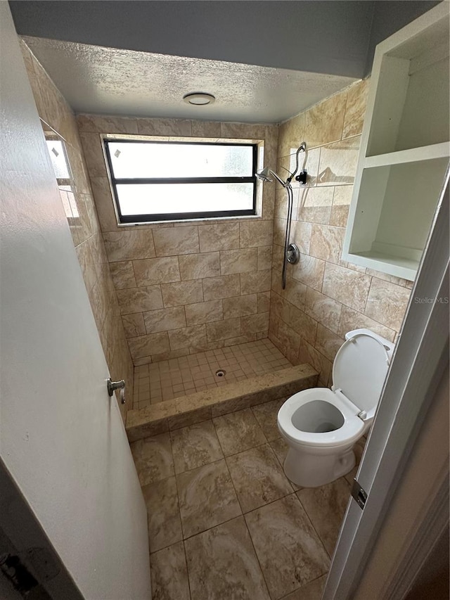 bathroom featuring toilet, tile patterned floors, plenty of natural light, and tiled shower