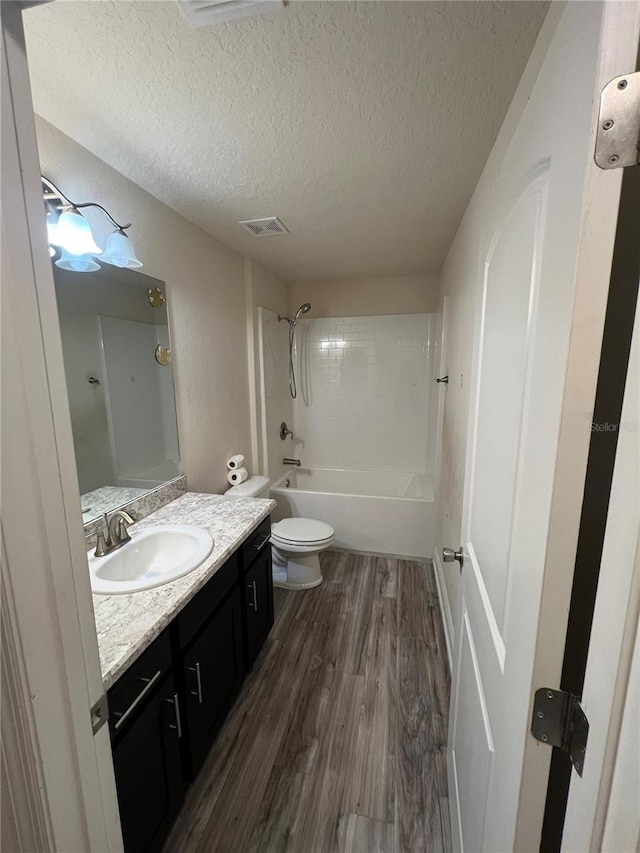 full bathroom featuring hardwood / wood-style floors, a textured ceiling, toilet, vanity, and bathtub / shower combination