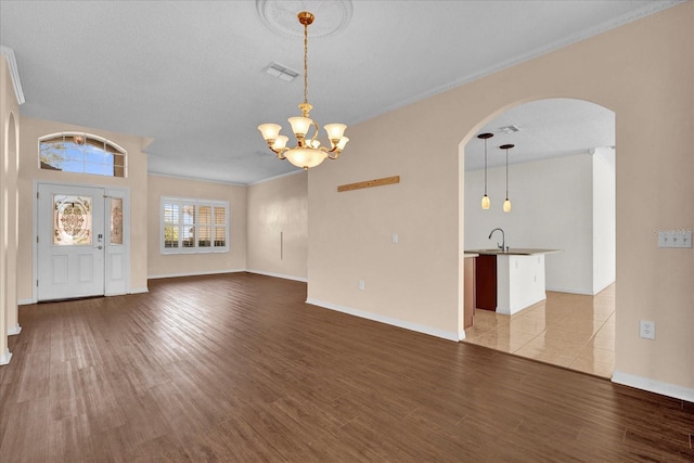 unfurnished living room featuring sink, a textured ceiling, light hardwood / wood-style floors, ornamental molding, and a chandelier