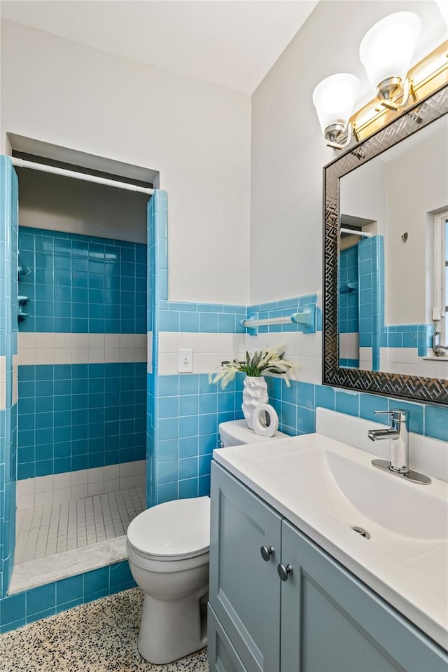 bathroom with toilet, tiled shower, tile walls, and vanity