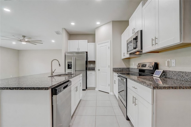 kitchen with appliances with stainless steel finishes, light tile patterned flooring, sink, white cabinets, and a kitchen island with sink