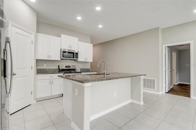 kitchen featuring an island with sink, stainless steel appliances, dark stone counters, sink, and white cabinetry