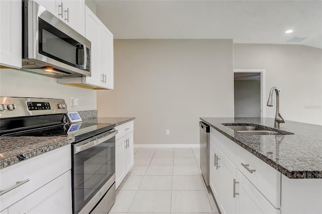 kitchen featuring white cabinets, light tile patterned floors, appliances with stainless steel finishes, dark stone counters, and sink