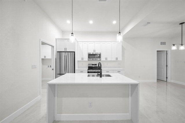 kitchen with appliances with stainless steel finishes, white cabinetry, sink, hanging light fixtures, and a center island with sink