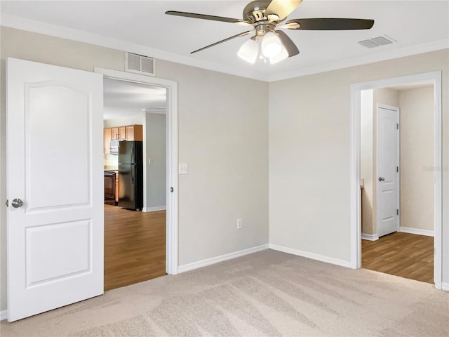 unfurnished bedroom with ceiling fan, light carpet, ornamental molding, and black fridge