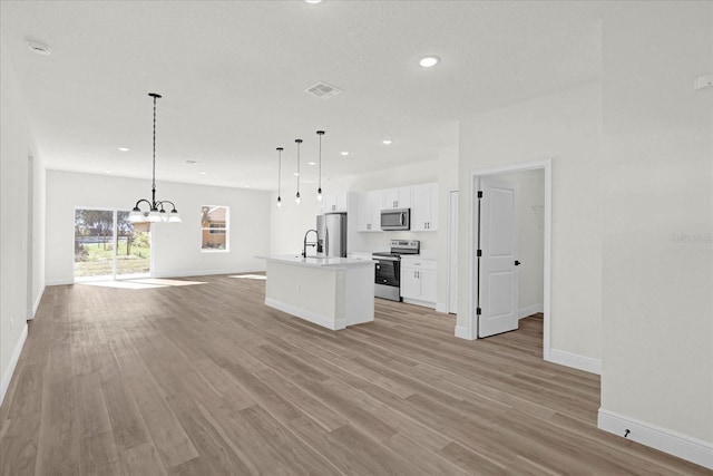 kitchen with stainless steel appliances, sink, white cabinets, hanging light fixtures, and a center island with sink