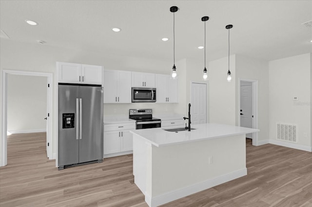 kitchen with decorative light fixtures, stainless steel appliances, a kitchen island with sink, white cabinets, and sink