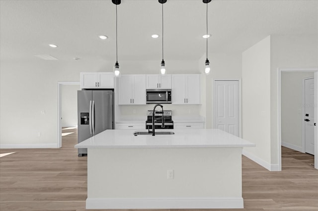 kitchen with hanging light fixtures, stainless steel appliances, an island with sink, white cabinetry, and sink