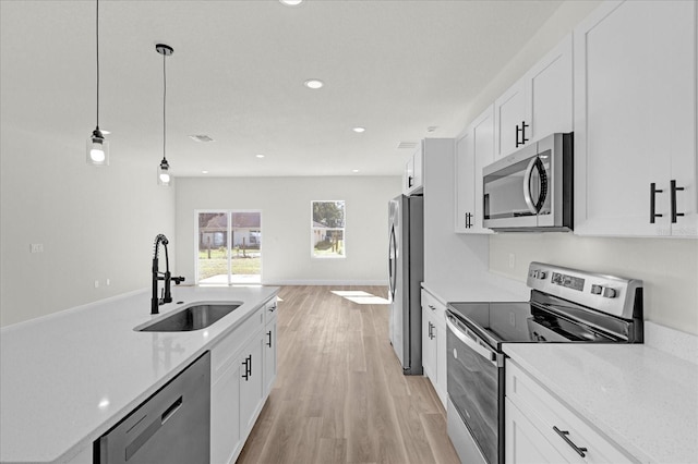 kitchen with appliances with stainless steel finishes, pendant lighting, white cabinets, light hardwood / wood-style flooring, and sink