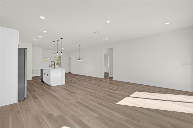 kitchen featuring a kitchen island with sink, pendant lighting, sink, light hardwood / wood-style flooring, and white cabinetry