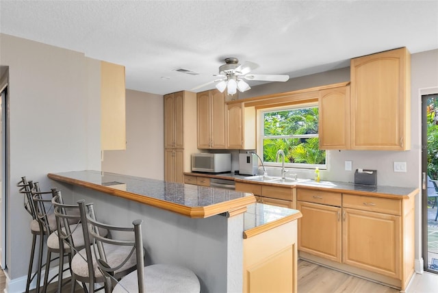 kitchen with light brown cabinetry, a breakfast bar, kitchen peninsula, and light hardwood / wood-style floors