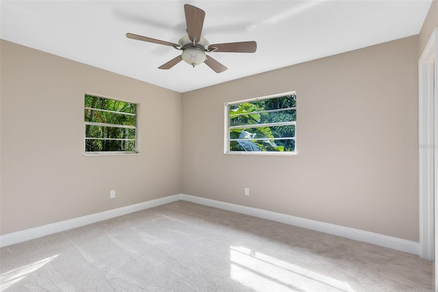 empty room featuring light colored carpet, baseboards, a ceiling fan, and a healthy amount of sunlight