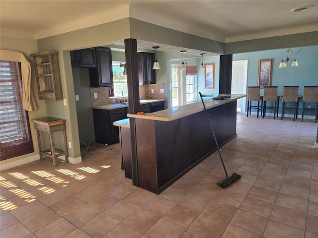 kitchen with a kitchen breakfast bar, dark brown cabinetry, pendant lighting, and an inviting chandelier