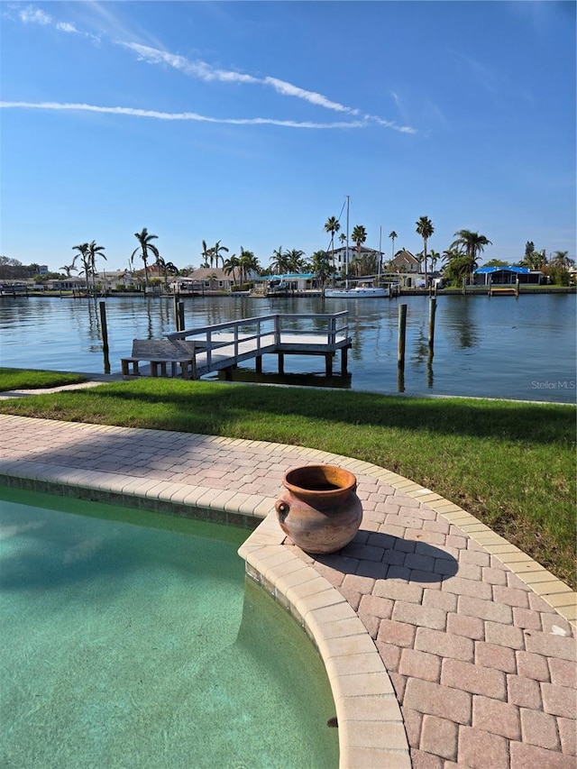 view of swimming pool featuring a water view, a dock, and a lawn