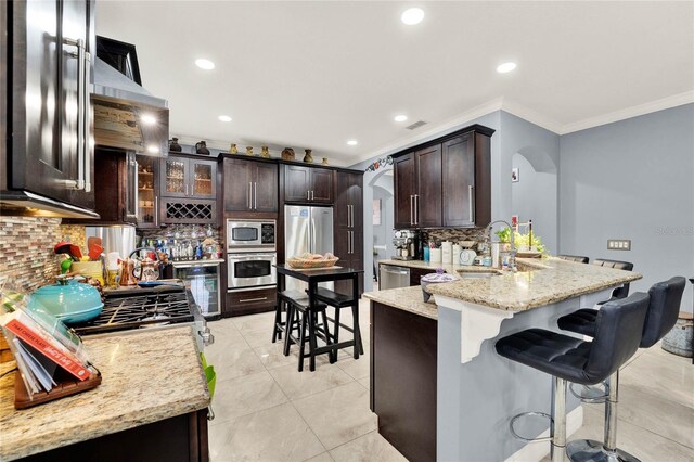 kitchen featuring stainless steel appliances, sink, a kitchen bar, light stone counters, and tasteful backsplash