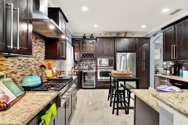 kitchen featuring crown molding, stainless steel appliances, dark brown cabinets, and light stone counters