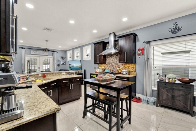 kitchen with french doors, wall chimney exhaust hood, sink, light stone countertops, and crown molding