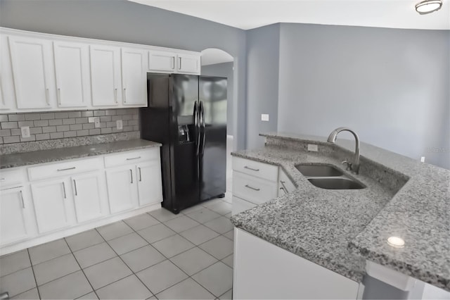 kitchen with black refrigerator with ice dispenser, white cabinets, light stone countertops, and tasteful backsplash