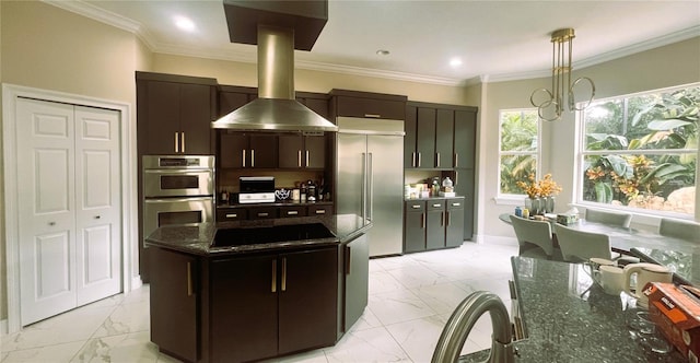 kitchen featuring dark brown cabinetry, hanging light fixtures, wall chimney range hood, dark stone counters, and appliances with stainless steel finishes