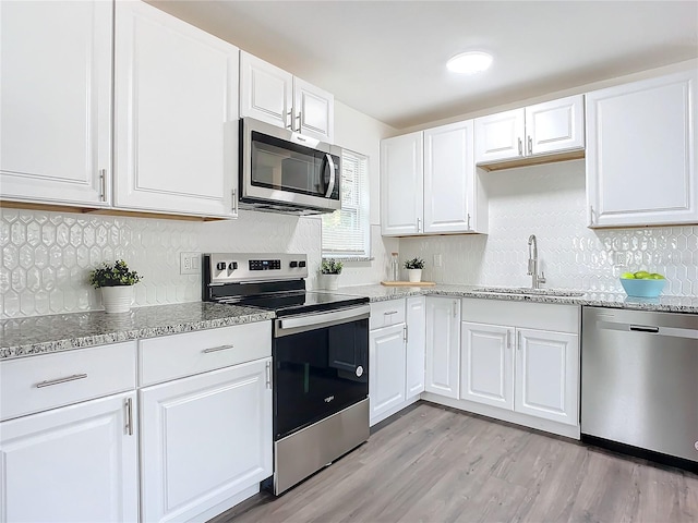 kitchen featuring white cabinets, appliances with stainless steel finishes, tasteful backsplash, light hardwood / wood-style floors, and sink