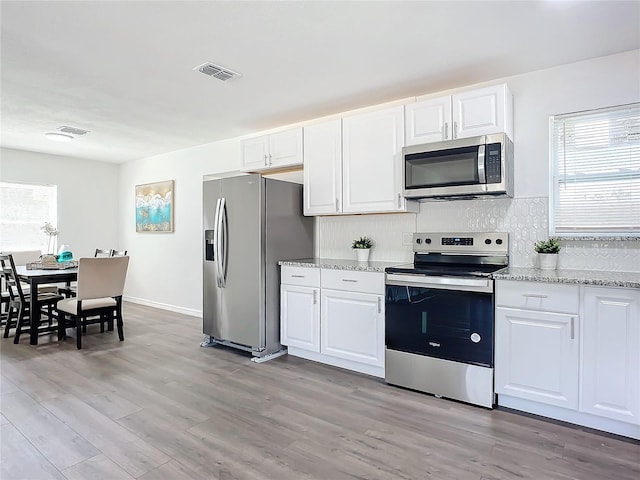 kitchen with appliances with stainless steel finishes, light hardwood / wood-style flooring, white cabinetry, and light stone countertops