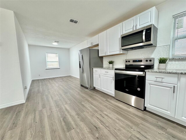 kitchen with backsplash, light wood-type flooring, stainless steel appliances, white cabinets, and light stone counters