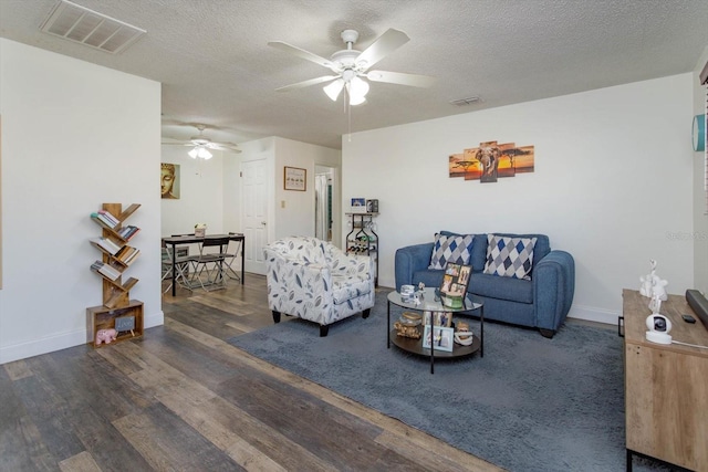 living room featuring dark wood-type flooring, ceiling fan, and a textured ceiling