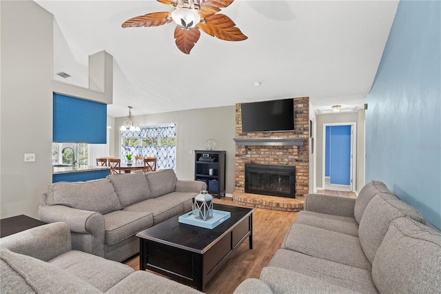 living room with wood-type flooring, sink, a brick fireplace, and ceiling fan with notable chandelier