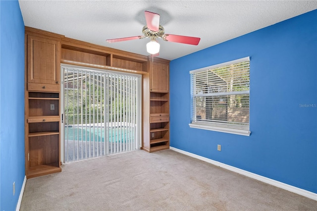 carpeted spare room with ceiling fan, a healthy amount of sunlight, and a textured ceiling