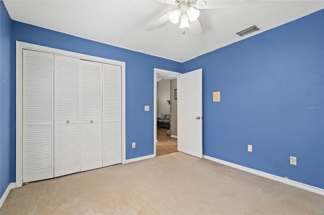 unfurnished bedroom featuring a closet, ceiling fan, light carpet, and a textured ceiling