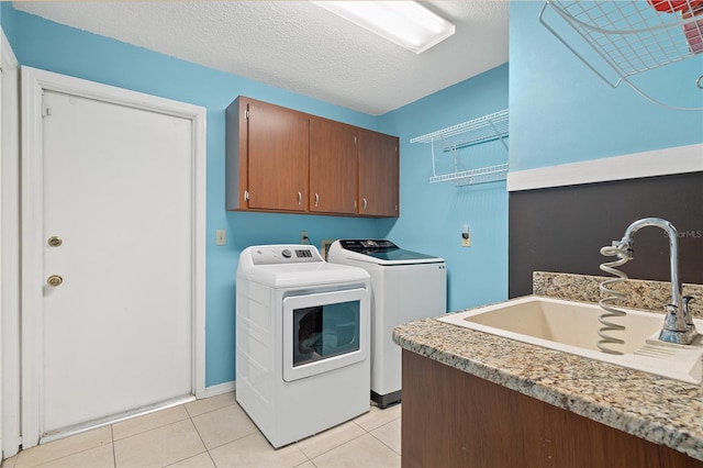 washroom featuring sink, light tile patterned floors, washing machine and dryer, a textured ceiling, and cabinets