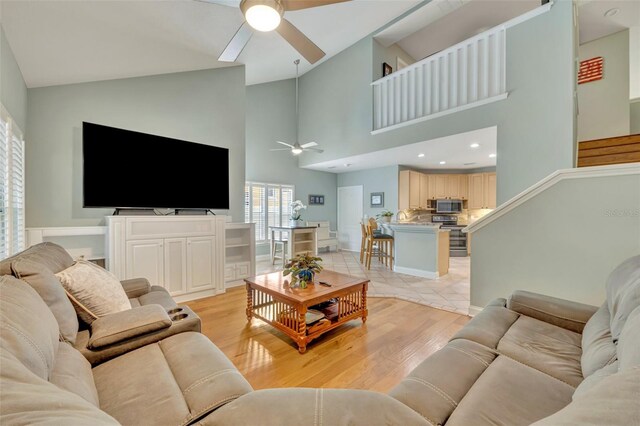living room featuring a ceiling fan, high vaulted ceiling, and light wood-style flooring