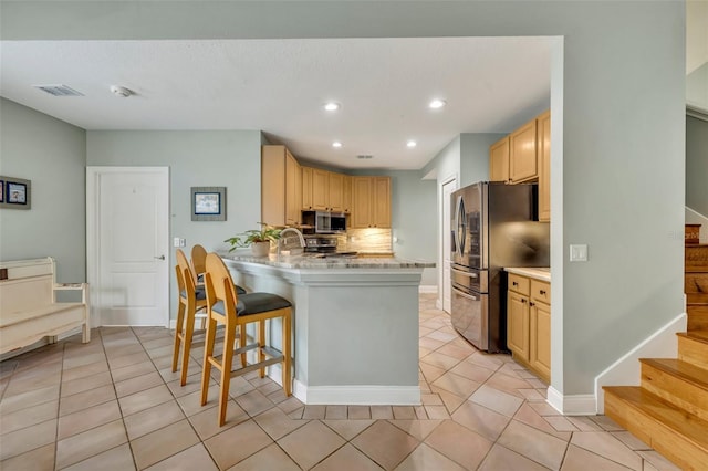 kitchen with kitchen peninsula, backsplash, a kitchen bar, light brown cabinetry, and appliances with stainless steel finishes