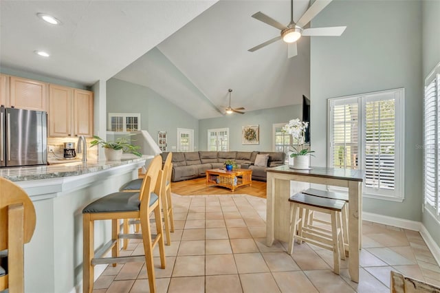 kitchen featuring freestanding refrigerator, light brown cabinetry, a breakfast bar, high vaulted ceiling, and a ceiling fan