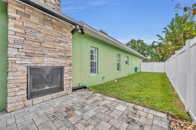 back of property with a patio area, an outdoor stone fireplace, a fenced backyard, stone siding, and stucco siding