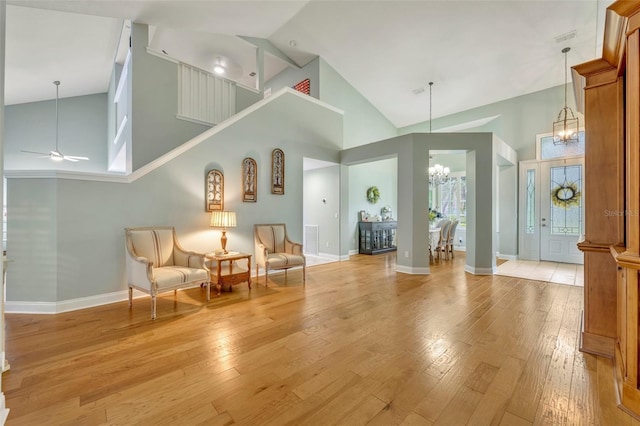 sitting room with ceiling fan with notable chandelier, light hardwood / wood-style flooring, and high vaulted ceiling