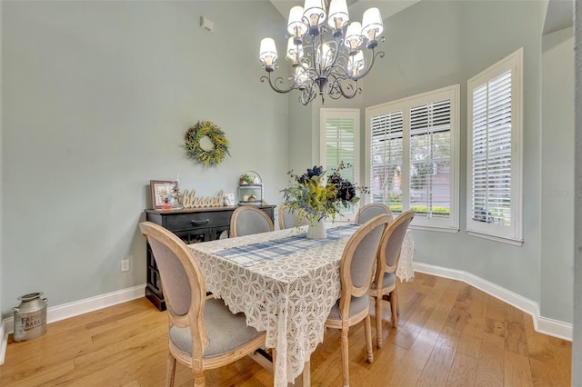 dining space featuring a notable chandelier, a towering ceiling, and light wood-type flooring