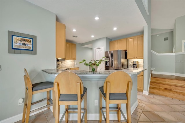 kitchen featuring a breakfast bar, kitchen peninsula, light brown cabinetry, and stainless steel fridge with ice dispenser