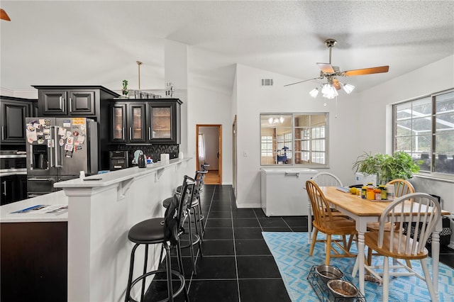 kitchen featuring lofted ceiling, ceiling fan, a kitchen breakfast bar, stainless steel fridge with ice dispenser, and dark tile patterned floors