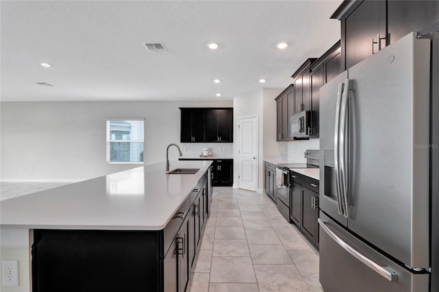 kitchen featuring light tile patterned flooring, sink, a center island with sink, a textured ceiling, and stainless steel appliances