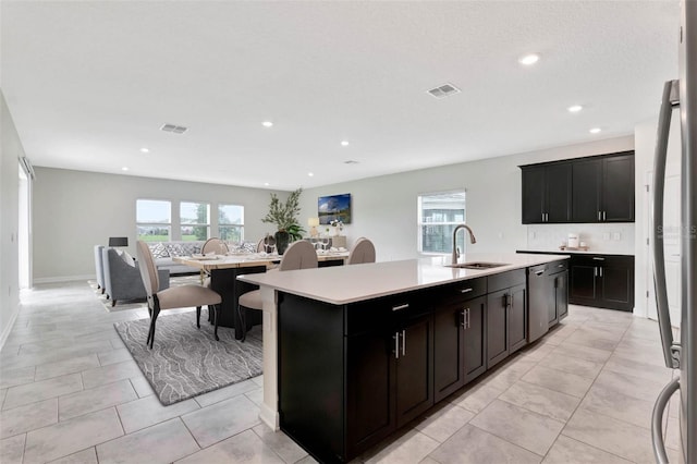 kitchen with light tile patterned flooring, stainless steel dishwasher, sink, and a center island with sink