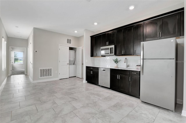 kitchen featuring tasteful backsplash, appliances with stainless steel finishes, stacked washer / dryer, and sink