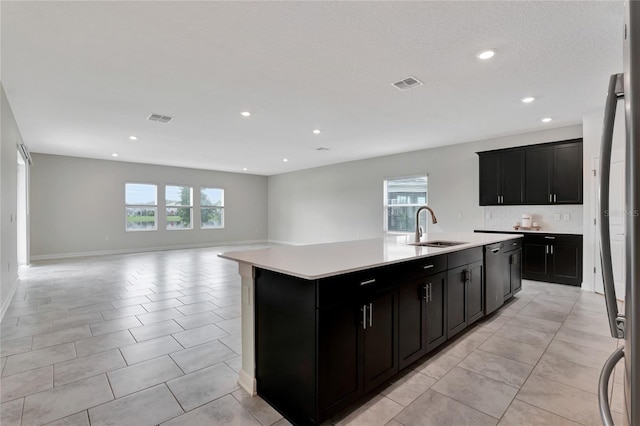 kitchen featuring a center island with sink, light countertops, visible vents, open floor plan, and a sink