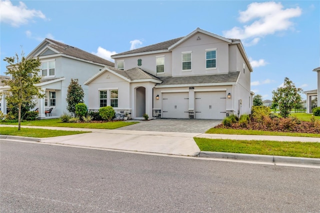 traditional-style house with a garage, decorative driveway, a front yard, and stucco siding