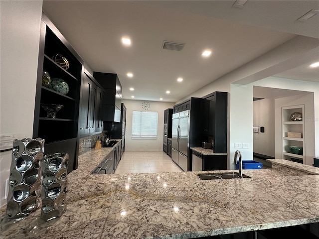 kitchen featuring sink, light stone counters, kitchen peninsula, stainless steel fridge, and built in features