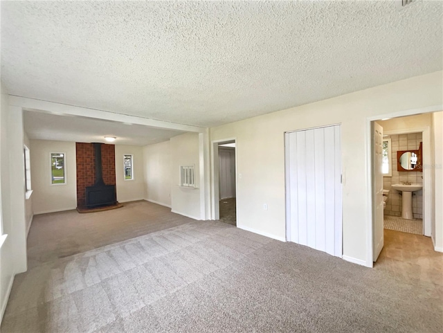 unfurnished bedroom featuring light carpet, a wood stove, sink, ensuite bathroom, and a textured ceiling