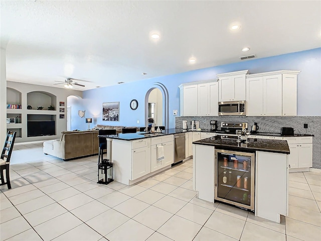 kitchen with a kitchen island with sink, stainless steel appliances, wine cooler, white cabinetry, and built in shelves