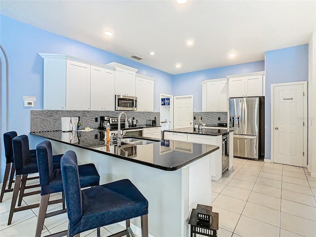 kitchen featuring kitchen peninsula, white cabinets, decorative backsplash, appliances with stainless steel finishes, and a kitchen breakfast bar