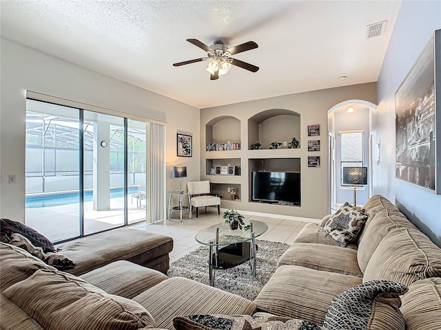 tiled living room featuring ceiling fan, built in features, and a textured ceiling