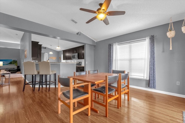 dining space with hardwood / wood-style floors, vaulted ceiling, a textured ceiling, and ceiling fan